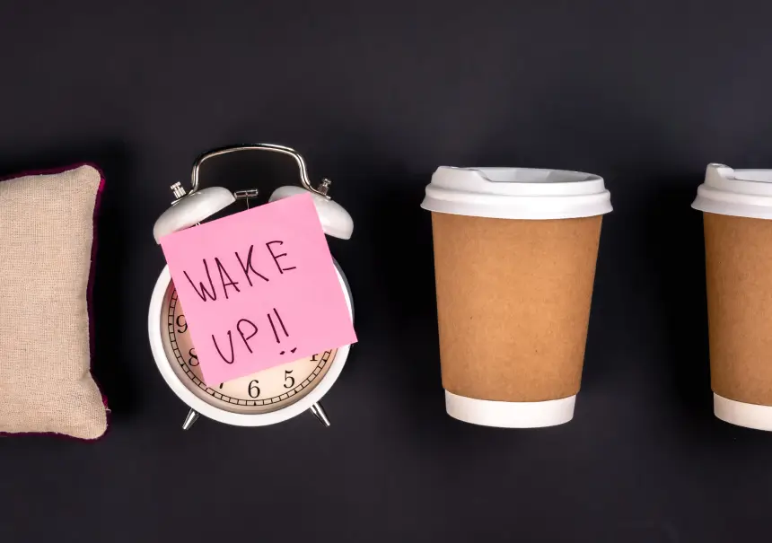 Budzik z karteczką „Wake up!!" obok poduszki i kubków kawy na ciemnym tle — ilustracja do artykułu o reaktywacji uśpionych leadów B2B