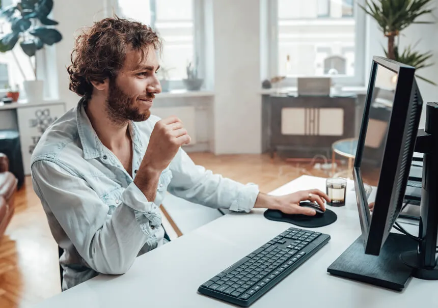 Użytkownik z uśmiechem przegląda stronę internetową i reaguje na dopasowany pop-up promocyjny. Mężczyzna w jasnej koszuli pracuje przy komputerze stacjonarnym w jasnym, nowoczesnym biurze.