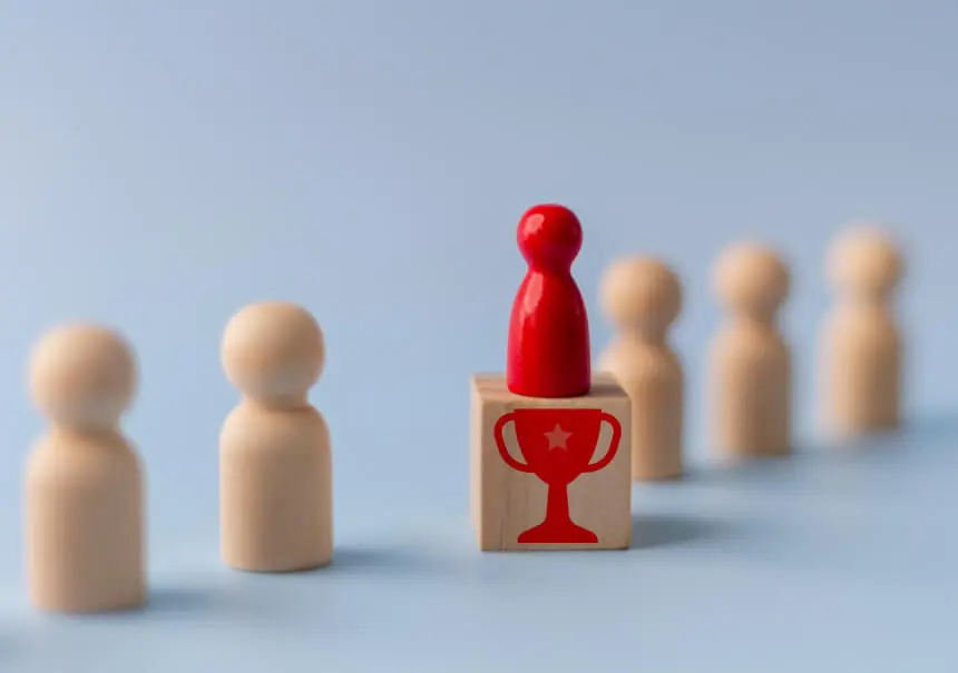 Lead scoring w automatyzacji marketingu – czerwony pionek symbolizujący wykwalifikowany lead stoi na drewnianym klocku z pucharowym nadrukiem, wyróżniając się na tle innych pionków.