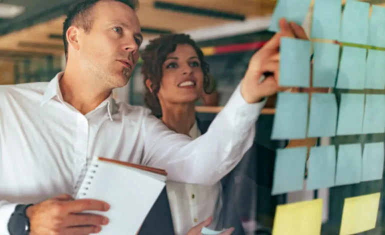 Zespół projektuje mapę podróży klienta (Customer Journey Mapping) pod kątem automatyzacji marketingu. Kobieta i mężczyzna przyklejają na szklanej tablicy karteczki reprezentujące punkty zetknięcia, scenariusze i triggery dla systemu.