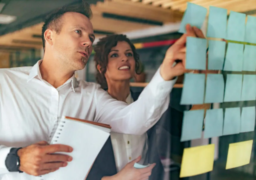 Zespół projektuje mapę podróży klienta (Customer Journey Mapping) pod kątem automatyzacji marketingu. Kobieta i mężczyzna przyklejają na szklanej tablicy karteczki reprezentujące punkty zetknięcia, scenariusze i triggery dla systemu.