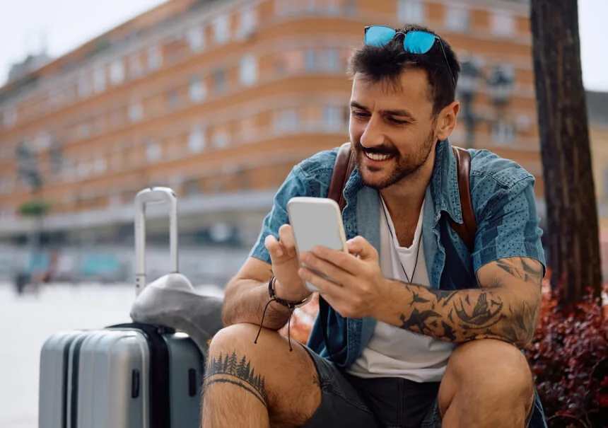 Uśmiechnięty podróżny czyta przypomnienie SMS o lotach i rezerwacji hotelu. Skuteczny SMS marketing w branży travel, usługi dla agencji turystycznych z Polski.