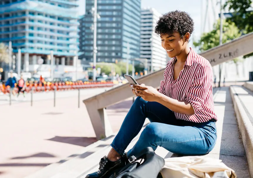 Uśmiechnięta klientka odczytuje na smartfonie promocyjny SMS ze sklepu internetowego, który skutecznie zachęca do powrotu do zakupów i zwiększa sprzedaż e-commerce.